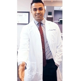 Male dentist in white coat and burgundy tie standing in dental office.