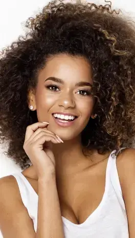 Smiling woman with curly hair wearing a white top in a dental practice portrait.